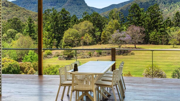 A wooden deck with a table and chairs, overlooking a lush green landscape and mountains.
