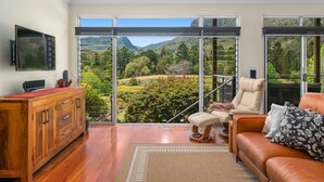 A modern living room with a wooden cabinet, a leather sofa, and a large sliding glass door offering a view of a mountainous landscape.