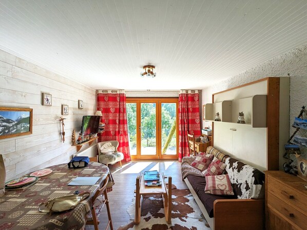 A cozy living room with a wooden ceiling, a sofa with patterned cushions, a dining table with a checkered tablecloth, and a view through the glass doors. - Apartment for 6, near slopes, terrace and parking in La Clusaz (La Clusaz)