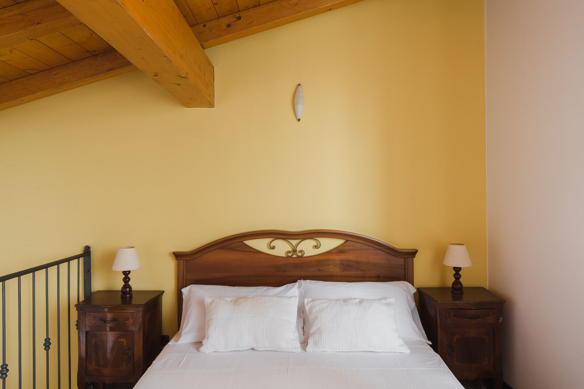 A bedroom with a wooden headboard, two bedside tables with lamps, and a single hanging light fixture.
