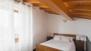 Un dormitorio con una cama de madera, dos mesitas de noche con lámparas, una ventana con cortinas traslúcidas y un techo inclinado.