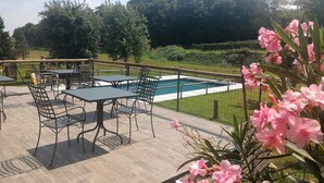 Un patio al aire libre con mesas y sillas, una piscina y follaje circundante.