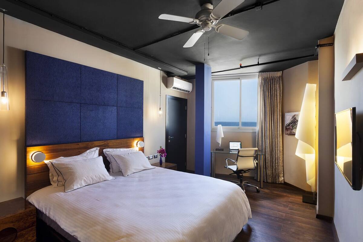 Camera d'albergo con un letto grande, una scrivania con un computer, una sedia e vista sul mare dalla finestra.
