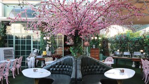 A garden patio with a black leather sofa, two round tables, and pink chairs. - TLV Port Boutique Residence (Tel Aviv)