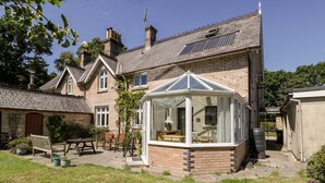 En traditionel murstensvilla med et orangeri, en patio med havemøbler og en have.