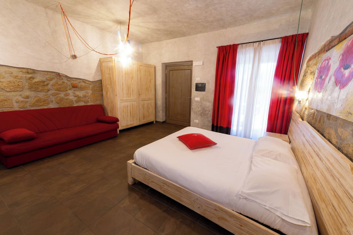 Ein Schlafzimmer mit einem hölzernen Bett, einem roten Sofa, einer Steinwand und einem Holzschrank.