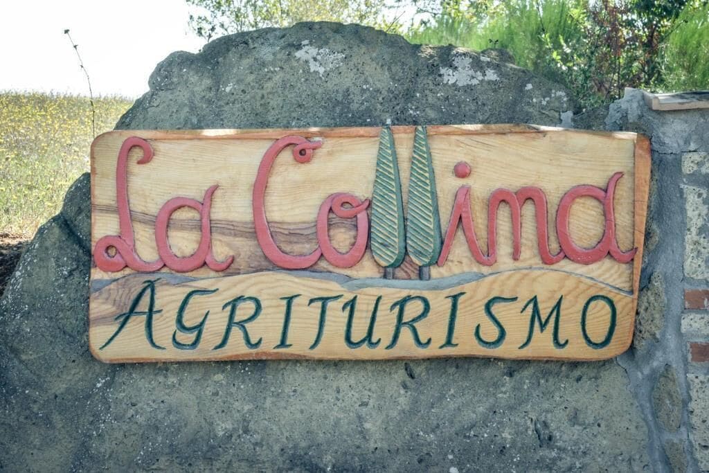 En träskylt med texten ”La Colina Agriturismo” mot en bakgrund av sten.