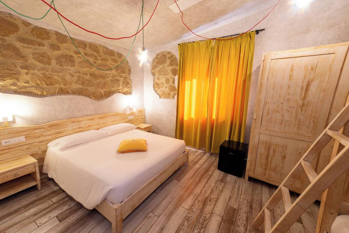 Ein Schlafzimmer mit einem hölzernen Bett, einer Steinwand und einem gelben Vorhang.