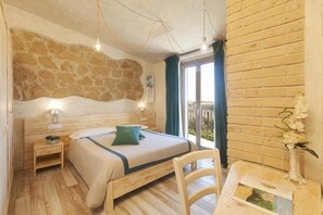 Un dormitorio acogedor con pared de piedra, cama de madera, mesita de noche, una silla y vistas al exterior.