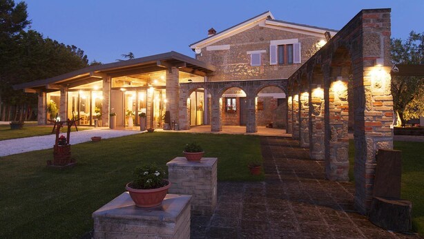 Un'ampia casa in pietra con portico coperto e diversi ingressi.