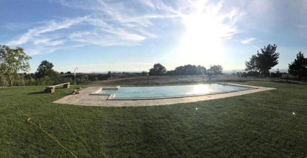 A rectangular swimming pool with a surrounding deck, surrounded by a grassy lawn and trees.
