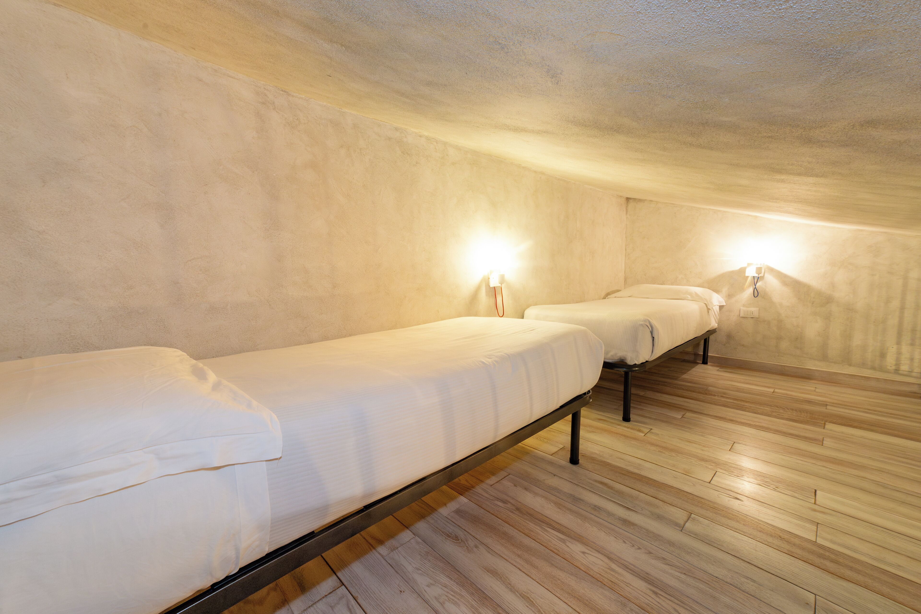 Varias camas individuales en una habitación con suelo de madera y paredes de color claro.