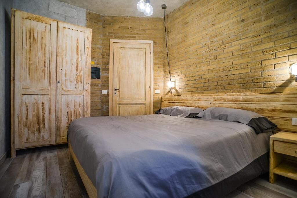 Ein Schlafzimmer mit hölzernem Kopfteil, einem Bett mit grauer Bettwäsche, einem Nachttisch und einem Holzschrank.