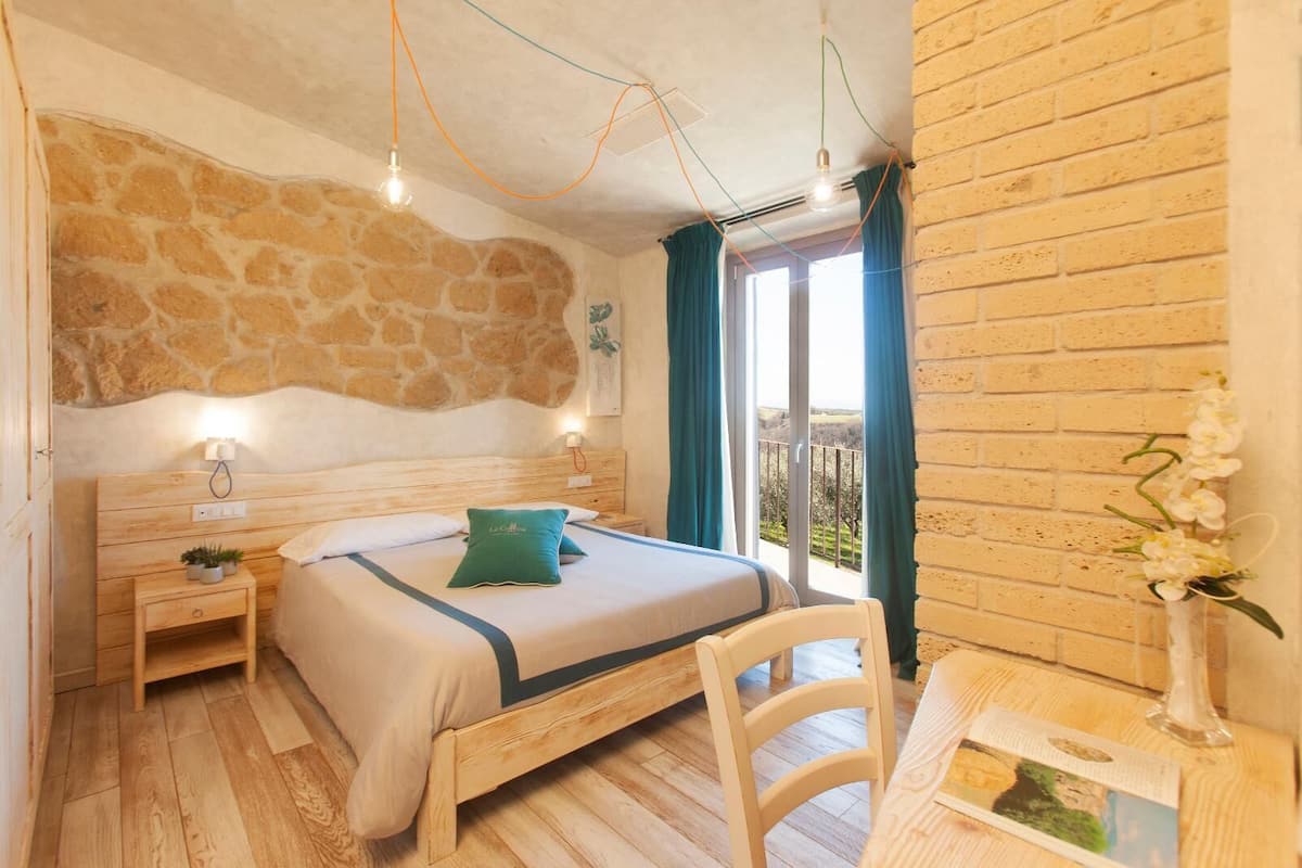 Ein Schlafzimmer mit Steinsandsteinwand, einem hölzernen Bett, Nachttischen, einem Sessel und Blick ins Freie.