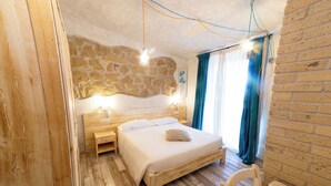 Una camera da letto con parete in pietra, pavimento in legno, un letto con lenzuola bianche, un comodino e una sedia.