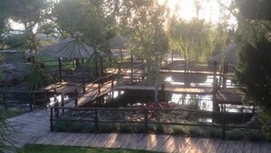 Un'elegante terrazza in legno con gazebo, circondata da vegetazione rigogliosa e un piccolo stagno.