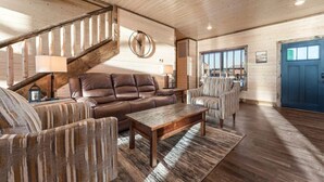 Un salon spacieux avec un escalier en bois, des canapés en cuir et une grande table basse en bois.