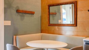 A corner seating area with a round table and two chairs, a wooden wall, a mirror, and a hanging light fixture.