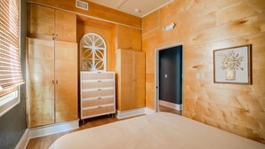 A bedroom with wooden walls, a large bed, a dresser, and a wardrobe.