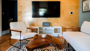 A modern living room with a flat-screen TV mounted on a wooden wall, a white sofa, a wooden coffee table, and a white armchair.