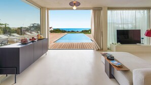 A modern living room with a pool view, a sofa, a TV, and a dining area with a table and chairs. - Stunning beachfront villa with pool and direct access to the sea in Sampieri - DiCasaInSicilia (Sampieri)