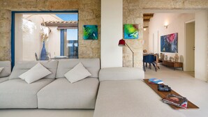 A modern living room with a stone wall, a sofa, a coffee table with magazines, and artwork on the walls. - Stunning beachfront villa with pool and direct access to the sea in Sampieri - DiCasaInSicilia (Sampieri)
