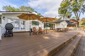 Eine Holzterrasse mit Gartenmöbeln, einem Grill und Sonnenschirmen.