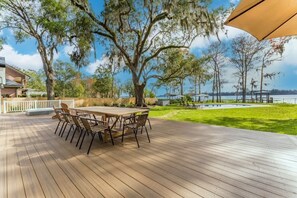 Um deck de madeira com mesa e cadeiras, cercado por árvores e vista para a água.