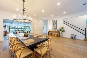 Uma ampla sala de jantar com uma mesa longa, cadeiras de vime e um lustre moderno.
