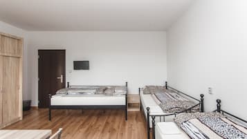 A bedroom with two beds, a wooden wardrobe, a small table, and a TV on the wall.
