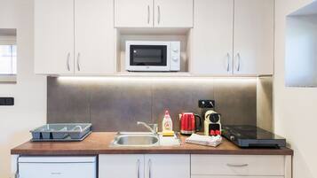A compact kitchen with white cabinets, a microwave, a coffee maker, and a toaster.