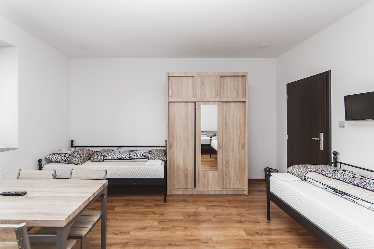 A bedroom with two beds, a wooden wardrobe, a TV, and a desk.