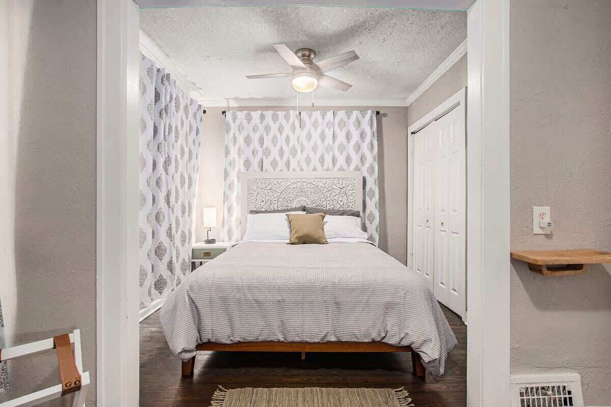 A bedroom with a bed, a ceiling fan, patterned curtains, and a bedside table.