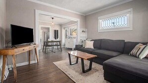 Ein Wohnzimmer mit einem dunkelgrauen Sofa, einem Holztisch, einem Fernseher auf einem Schrank und einem gemusterten Teppich.