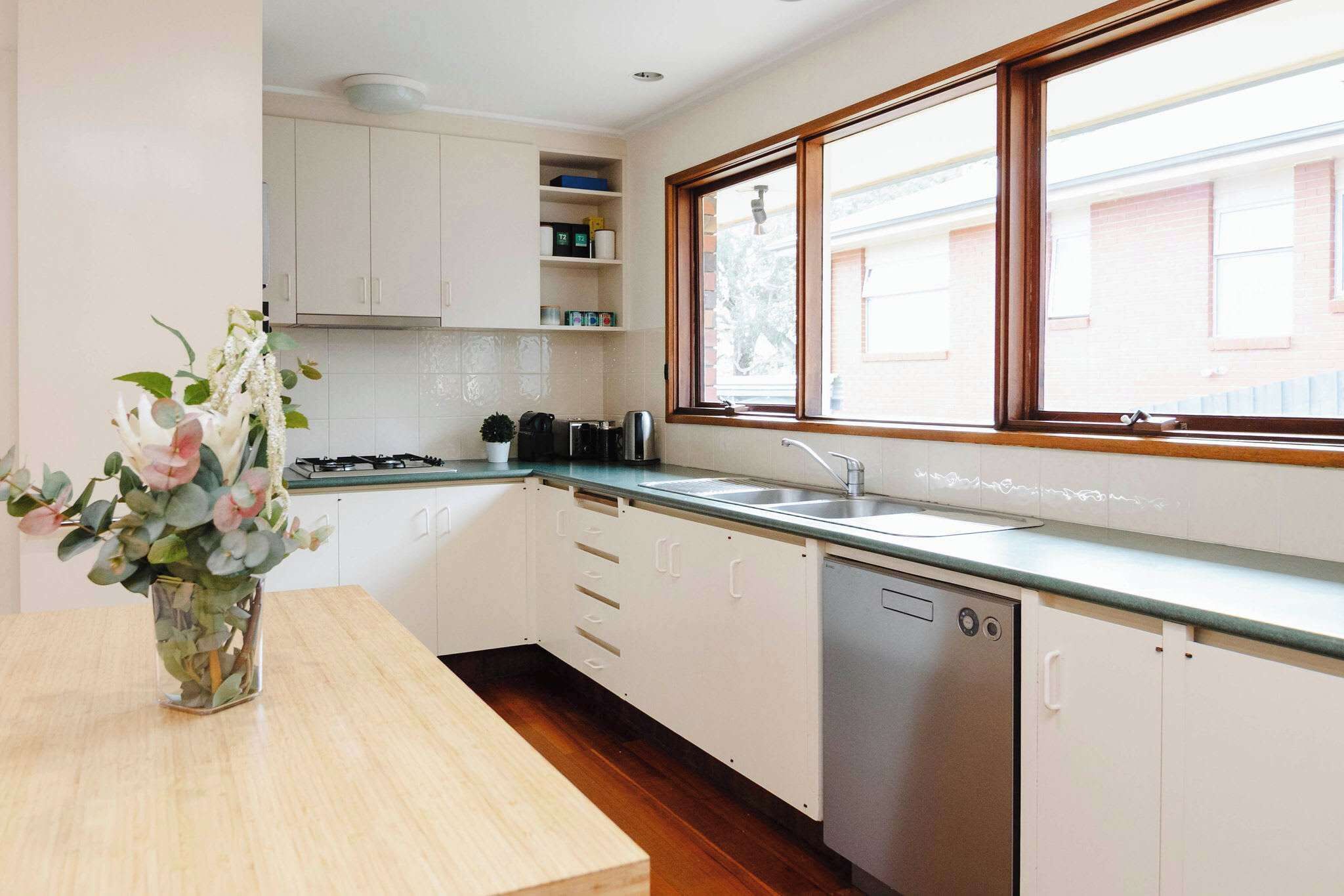 Una cocina moderna con armarios blancos, lavavajillas, pileta y ventana con vista a edificios.