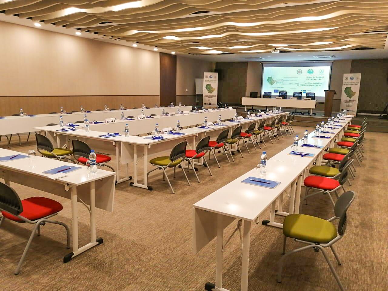 A conference room with multiple tables, chairs, and a presentation screen.