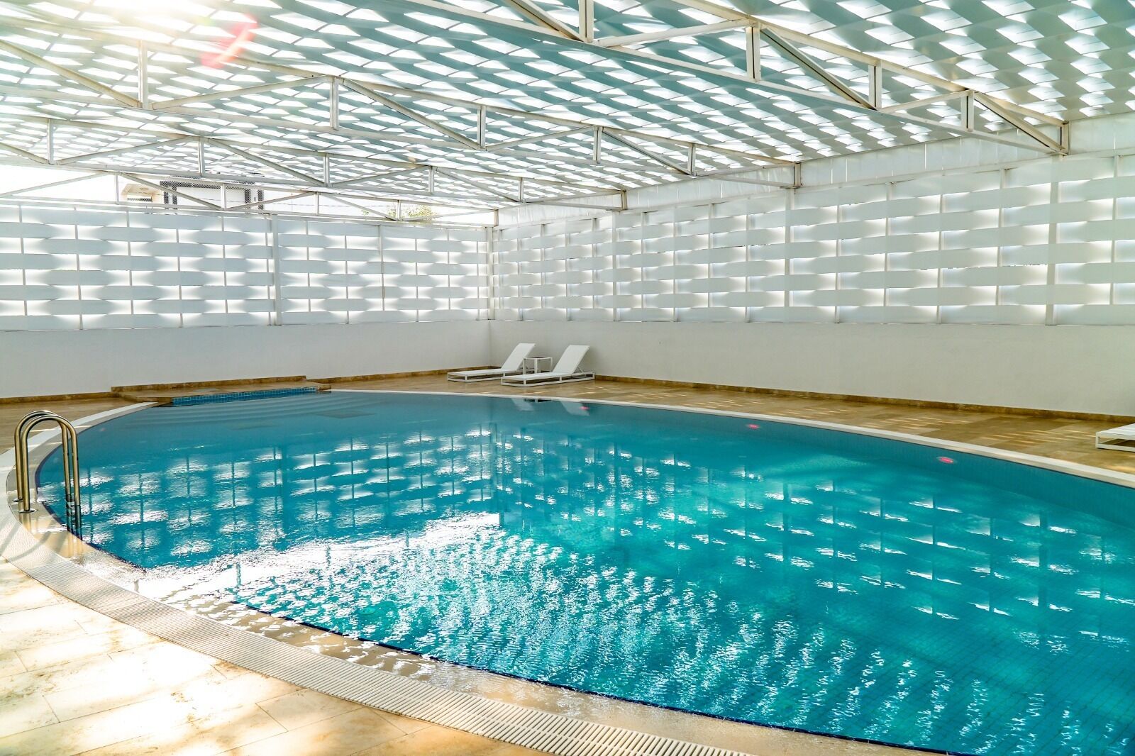 An indoor swimming pool with clear water, a tiled floor, and a ceiling with a geometric pattern of white panels.