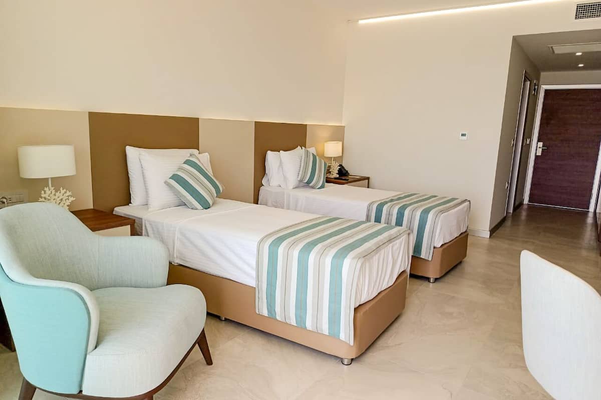 Ein Hotelzimmer mit zwei Betten, einer Sitzecke und einer Tür zu einem Flur.