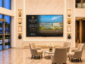 A modern hotel lobby with a large screen displaying the resort's name and views, comfortable seating, and decorative vases. - GADILEH RESORT HOTEL (Tadjoura)