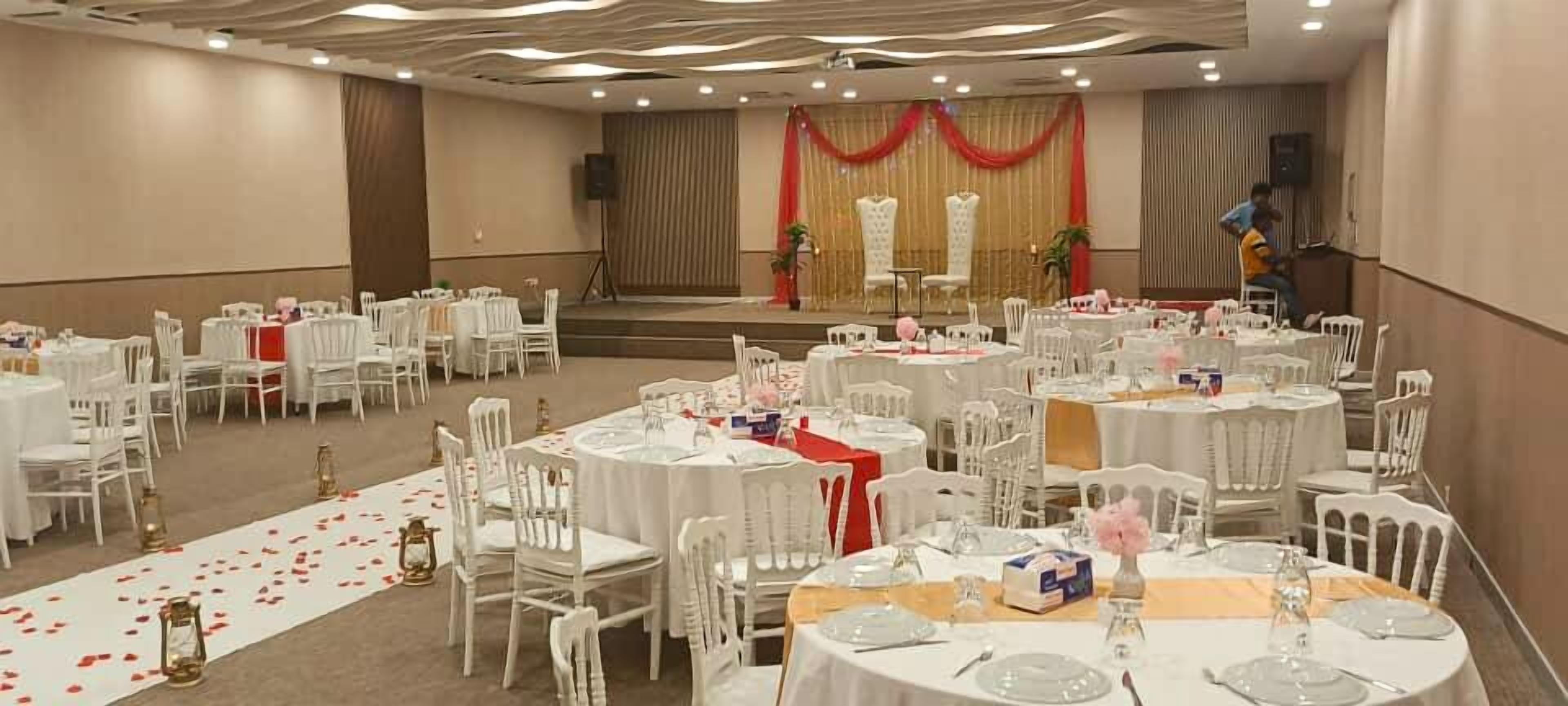 A banquet hall with round tables, chairs, and a stage with red curtains.