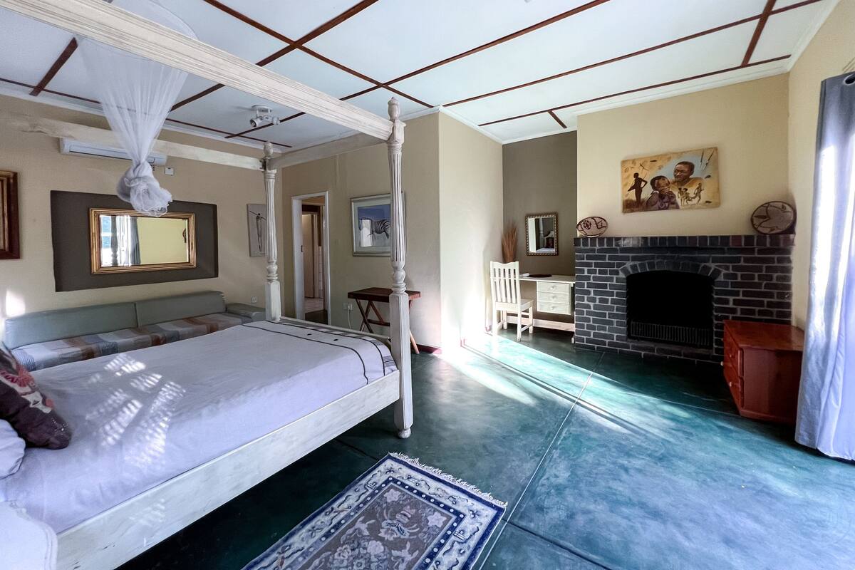 A bedroom with a four-poster bed, a desk, a chair, a fireplace, and a large mirror.