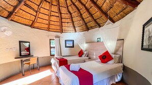 Una habitación con dos camas, un escritorio, una silla, un ventanal y un techo de paja.