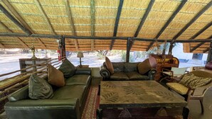 Un área de estar al aire libre con techo de paja, sofás de cuero y un reposapiés estampado.
