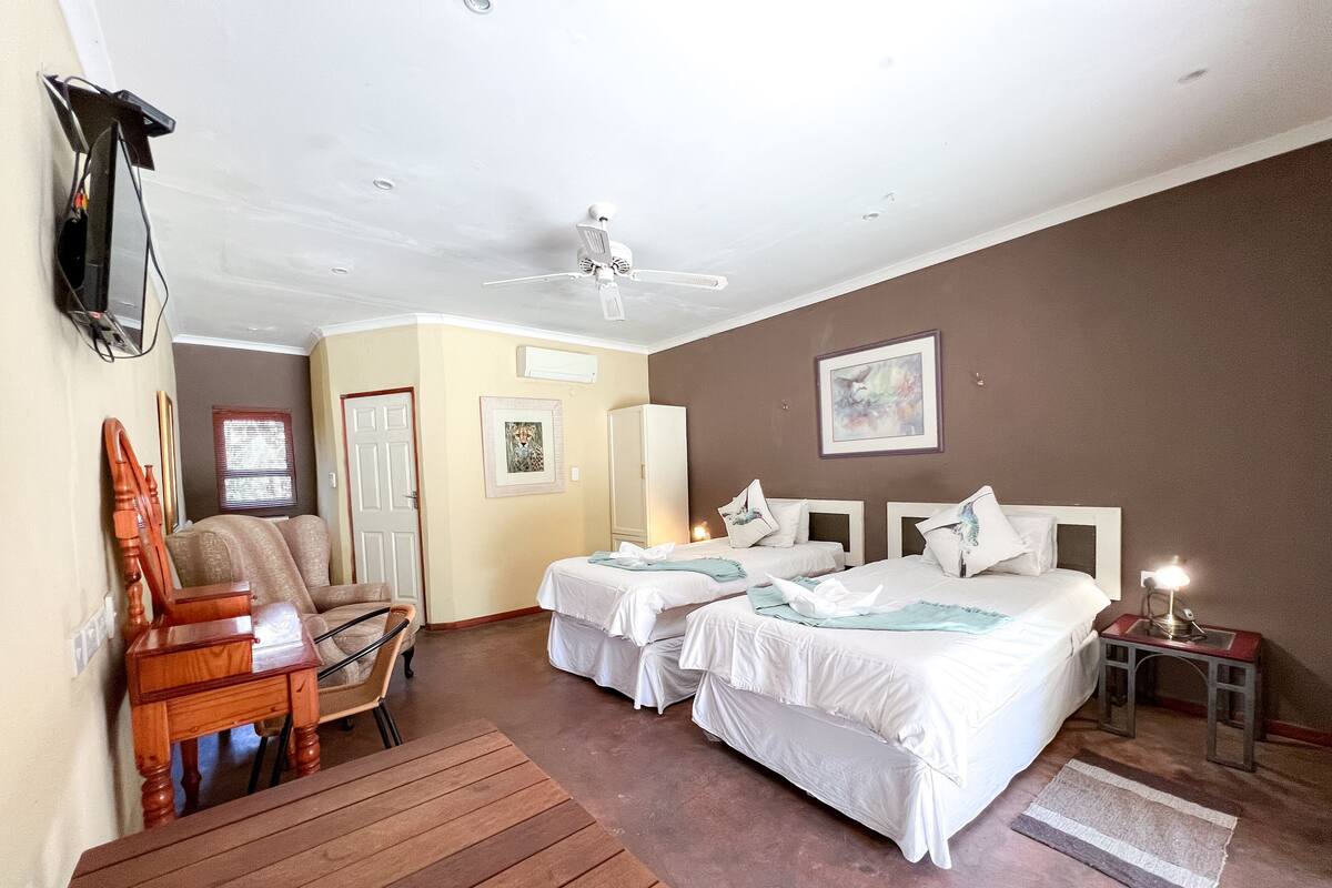 A hotel room with two beds, a wooden chair, a desk, and a ceiling fan.