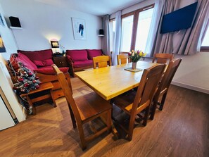 A cozy living room with a wooden dining table, red sofa, and a small Christmas tree.