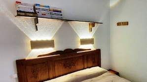 A bedroom with a wooden headboard, a bed with a patterned bedspread, and two wall-mounted reading lights.
