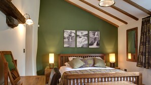 A bedroom with a wooden bed, two bedside tables with lamps, a wooden bench, and three framed pictures on the wall. - Neddy House (Richmond)