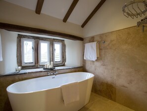 A bathroom with a freestanding bathtub, two windows with curtains, a towel rack, and stone walls. - Neddy House (Richmond)