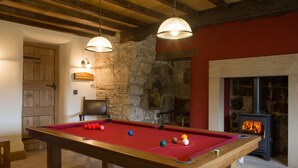 A pool table with balls, a stone wall, a fireplace, and wooden beams. - Neddy House (Richmond)