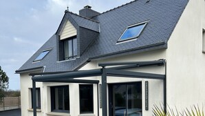 Ein modernes Haus mit überdachter Terrasse, einem Swimmingpool und einem gepflegten Rasen.